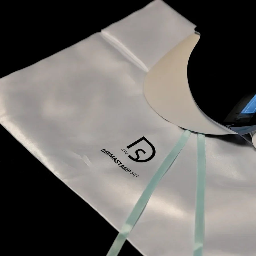 Den vita förvaringspåsen i satin med logotypen dermastamp.hu, med masken liggande på den
