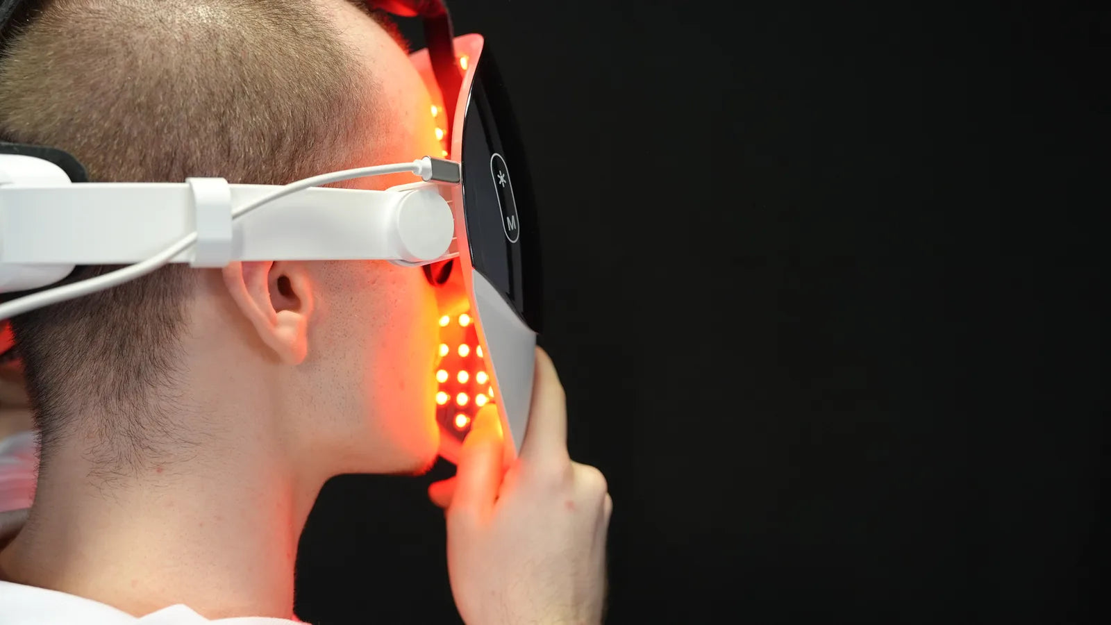 LED-mask med stel stomme under användning, från sidan: LED-skivan rör inte vid huden, det röda ljuset syns på kindbenet